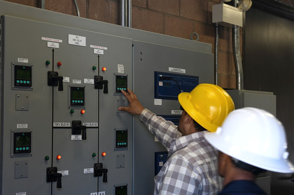 Two technicians reviewing settings on an electrical control panel