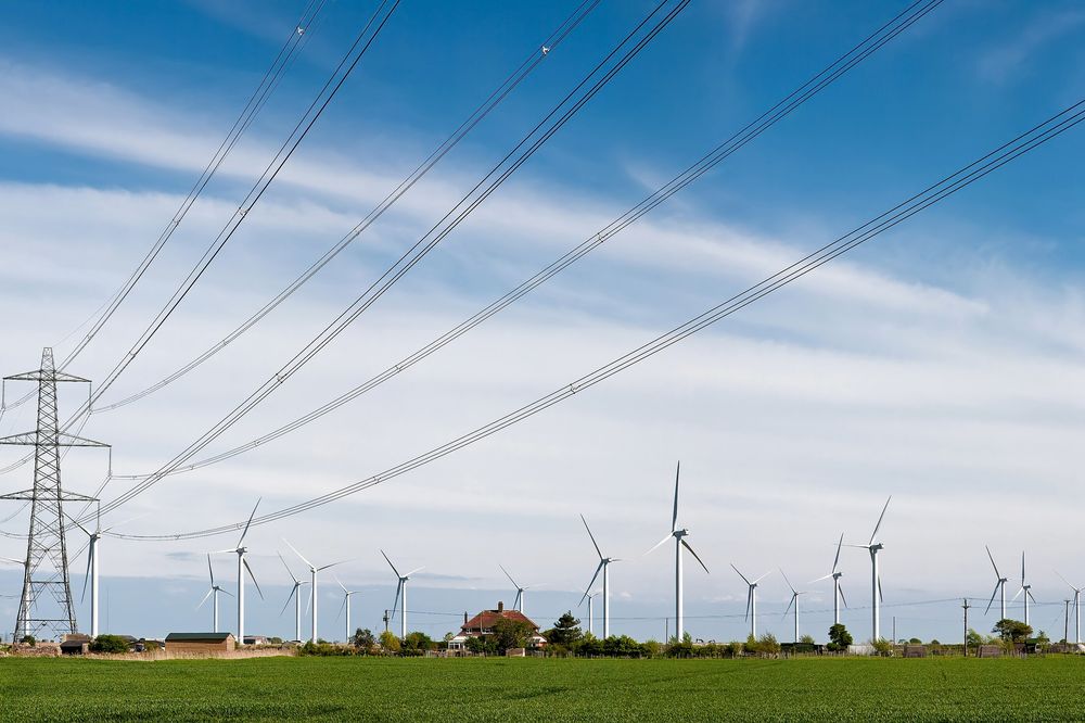 Transmission lines crossing farmland with wind turbines behind