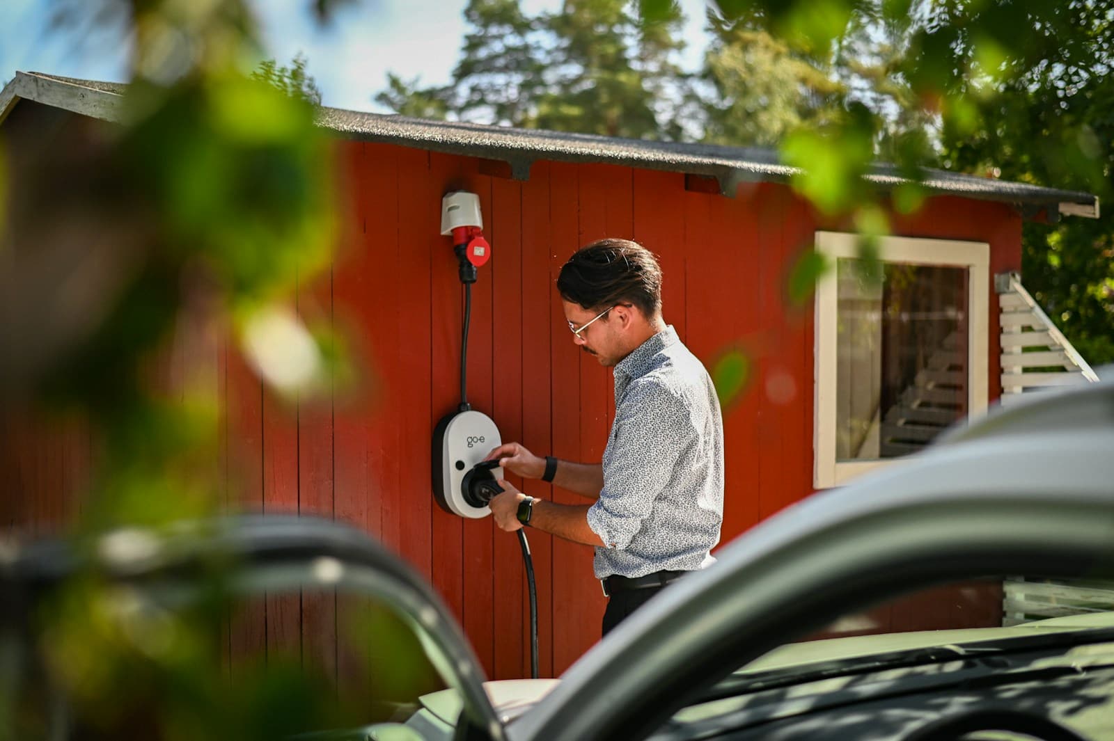 Technician connecting a cable to a wall-mounted AC charging unit outside a building
