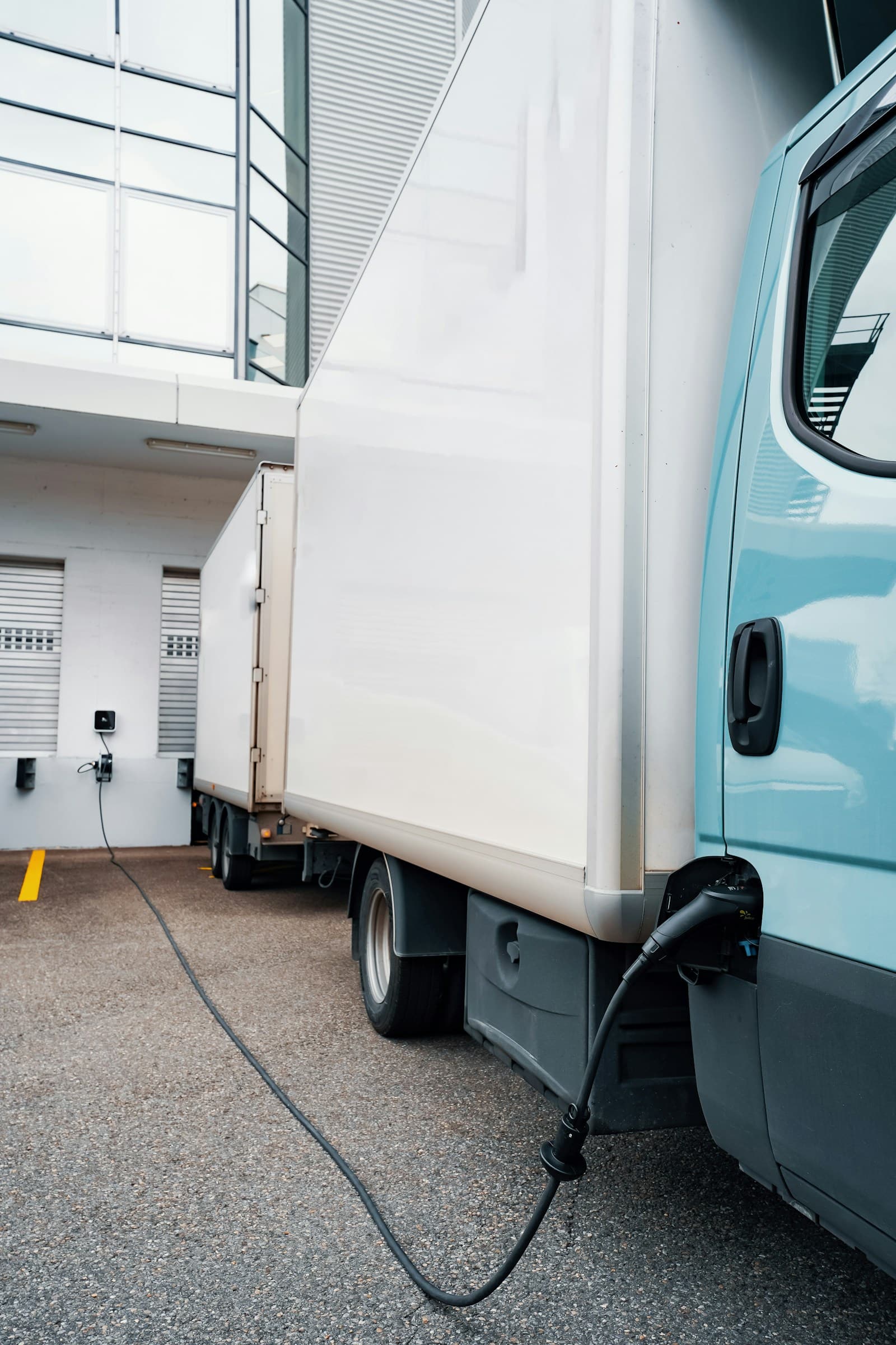 Electric delivery truck connected to a depot charger beside a loading bay
