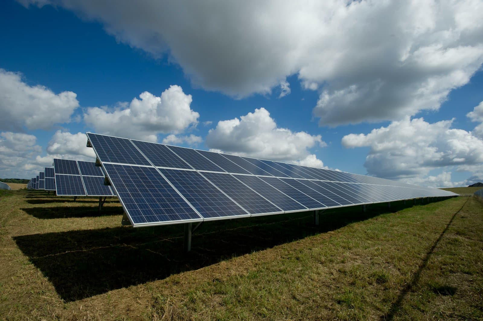 Rows of solar panels in an open field under a bright, clouded sky